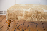 Vintage Oushak rug ottoman, showing textured cream pile, hand-sewn edge, and turned wood leg.