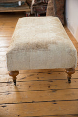 Curved wooden leg with brass caster on the vintage Oushak rug ottoman.