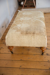 Textured cream Oushak rug fragment on vintage ottoman, featuring hand-sewn corner.