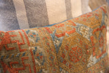 Aged Belouch rug fragment pillow, showing geometric tribal patterns in terracotta, blue, and golden-brown.