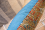 Textured antique Belouch rug fragment pattern in rust and gold, beside solid blue fabric.
