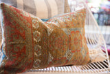 Worn, textured pile with geometric rust, teal, and gold patterns on the antique Belouch pillow.