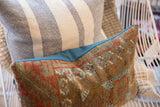 Aged Belouch rug fragment pillow's intricate geometric pattern, earthy tones, and teal piping.