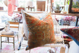 Antique Belouch fragment pillow, intricate geometric design, aged hand-knotted texture in warm orange, olive, blue.