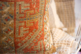 Close-up of antique Belouch fragment pillow's aged texture, terracotta and gold geometric weave.