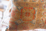 Aged texture and geometric patterns in rust, blue, and tan on an antique Belouch pillow.