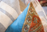 Close-up of antique Belouch rug pillow, geometric pattern in warm tones, contrasted by bright blue textile.