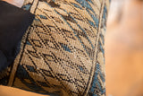 Vintage Caucasian rug lumbar pillow with distressed tan, blue, brown geometric pattern and black fabric edge.