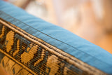 Geometric tan and dark blue vintage Caucasian rug fragment, light blue fabric backing.