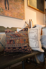 Bottom border of antique Afshar rug fragment pillow, dark blue with geometric patterns in rust and beige.