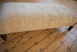 Distressed vintage Persian rug ottoman, highlighting faded neutral colors and subtle motifs.