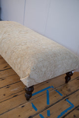 Distressed vintage Persian rug fragment texture with subtle neutral patterns on ottoman.