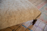 Distressed vintage Persian rug fragment covering the ottoman side, with faded neutral patterns.
