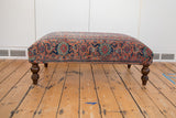 Dark turned wooden legs supporting the vintage Persian rug ottoman.