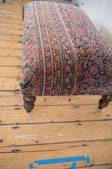 Vintage Persian rug fragment ottoman side showing red, navy patterns, and turned leg.