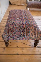 Vintage Persian rug ottoman end, featuring ornate navy, faded red, gold patterns and turned leg.
