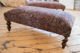Vintage Persian rug ottoman corner with intricate navy, faded red pattern, and dark carved leg.