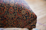 Vintage Persian rug fragment with ornate navy, faded red, gold pattern on ottoman corner.