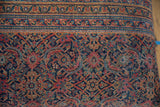 Close-up of vintage Persian rug fragment, showing border and dense patterns in faded red, navy, and teal.