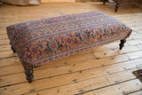 Vintage Persian rug ottoman with intricate floral pattern in faded red, navy, gold.