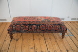 Full surface of vintage Persian rug ottoman revealing rich, aged patterns and dark wood legs.