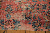 Aged Persian rug fragment shows rose red, navy floral motifs with visible foundation.