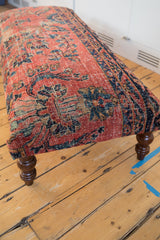Dark carved wooden leg and patterned base edge of the vintage rug ottoman.