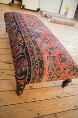 Dark turned leg and corner of the vintage Persian rug upholstered ottoman.
