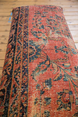 Vintage Persian rug fragment detail: intricate rose red, navy, gold floral pattern, time-softened texture.