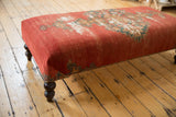 Turned dark wooden leg and patterned side of the antique rug ottoman.