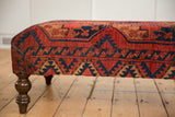 Side view: Antique Ersari rug fragment ottoman with red, navy geometric pattern, turned leg.