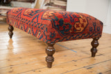 Angled end of antique Ersari rug fragment ottoman, with bold red, navy geometric design.