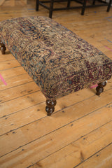 Antique Persian Kerman rug ottoman, featuring worn texture and faded beige, blue, red patterns.