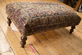 Turned dark wood leg and beige, red patterned side of the antique Kerman rug ottoman.