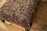 Antique Kerman rug fragment on ottoman, beige, ruby, cobalt patterns, worn pile to foundation.