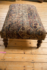 Dark carved wooden leg detail with antique Persian rug fragment showing knothead wear.