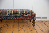Side of vintage ottoman displaying Northwest Persian rug fragment with geometric red, teal, navy patterns.