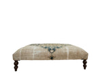 Antique rug ottoman side panel with dusty navy pattern, distressed beige, and dark curved leg.