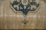 Antique Persian rug fragment detail: dusty navy floral pattern on worn beige field, foundation visible.