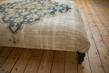 Ottoman lower side with antique beige rug fragment, isolated wear, and dark wooden leg.
