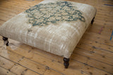 Side detail of the Antique Persian Doroksh rug ottoman, revealing its worn texture and dark carved leg.
