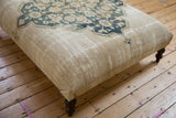 Ottoman table side showcasing textured antique ivory plain weave with a dark wooden leg.