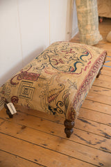 SKU tag and dark turned leg detail of the antique Persian rug fragment ottoman table.
