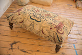 Dark turned wooden leg of the antique rug fragment ottoman table on wood floor.