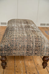 Visible worn texture and faded slate gray, beige, and charcoal motifs on rug fragment ottoman.