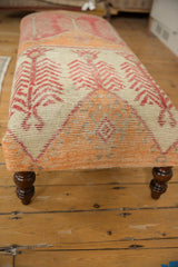 Ottoman side showing tangerine distressed rug fragment, dusty rose pattern, and curved wooden leg.