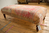 Textured side view of vintage rug fragment ottoman, with distressed tangerine and rose patterns.
