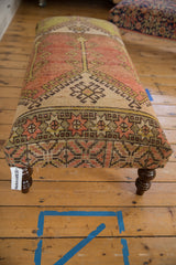 Faded red, green geometric pattern on vintage Oushak ottoman with curved dark wood leg.