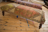 Dark carved wooden leg of a vintage rug ottoman, with white tag.