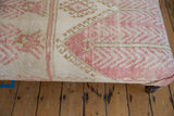 Close-up of distressed vintage Oushak rug fragment, blush pink, ivory, and tan geometric patterns.